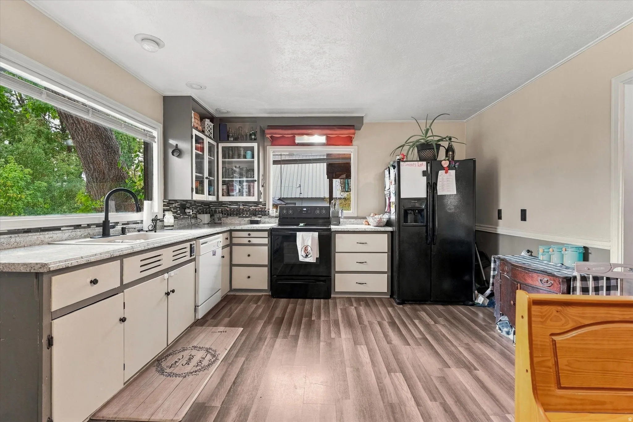 Kitchen featuring wood-finish flooring, a large window, granite-style countertops, and a full suite of black appliances