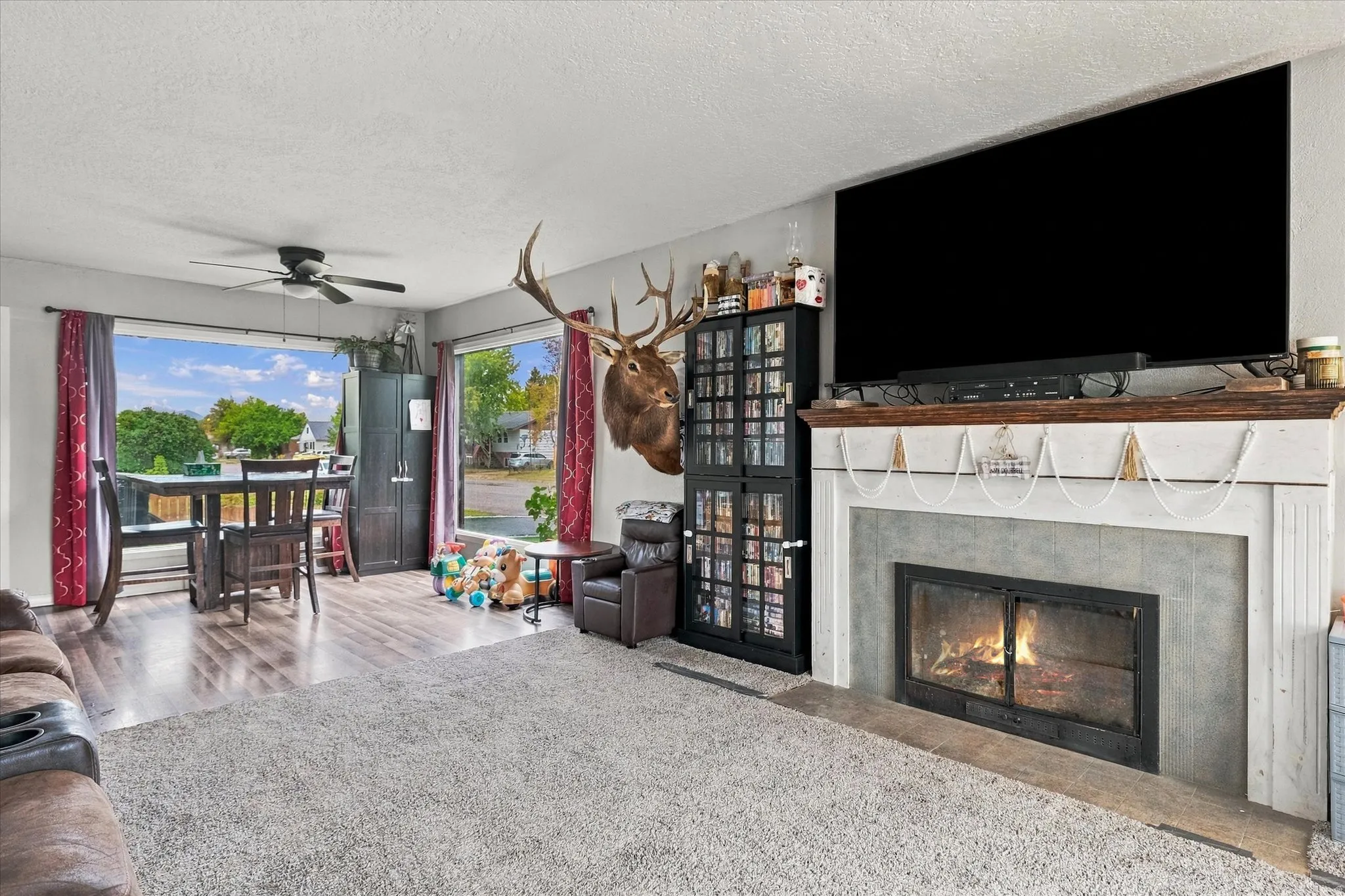 Living area featuring a fireplace with a stone surround and wood mantel, large window, and ceiling fan