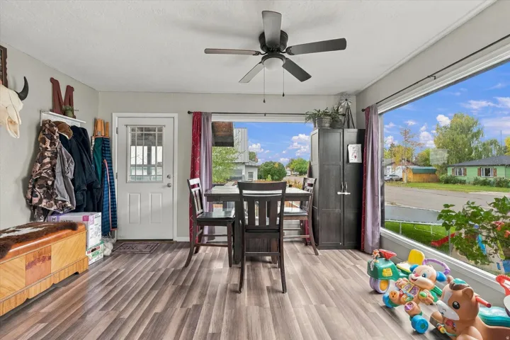 Wood-finish flooring throughout, ceiling fan with integrated lighting, white paneled door with window, and expansive window offering abundant natural light