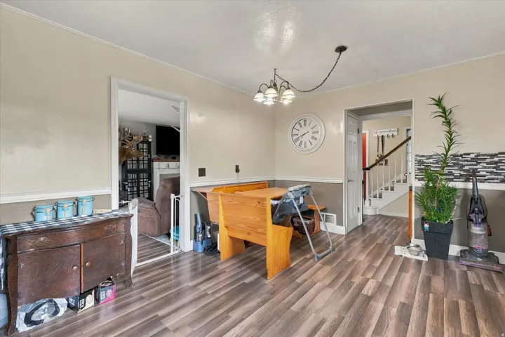 Wood-finish flooring, accent wall with decorative tile, chair rail molding, and a staircase with white risers and dark handrail