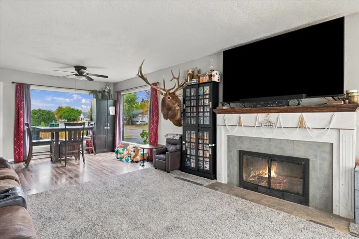 Living area featuring a fireplace with a stone surround and wood mantel, large window, and ceiling fan