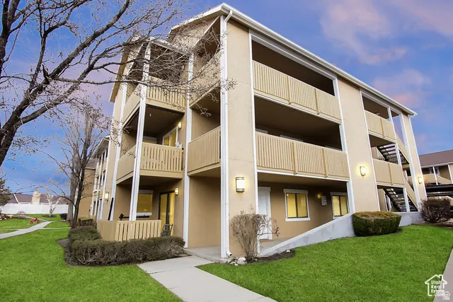 Multi-story building featuring balconies, exterior lighting fixtures, and a landscaped green space