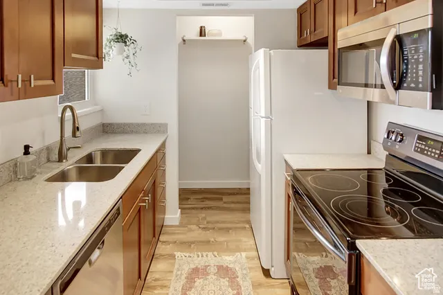 Galley kitchen featuring wood-finish cabinetry, light-toned countertops, a double basin sink with a brushed nickel faucet, and stainless steel appliances