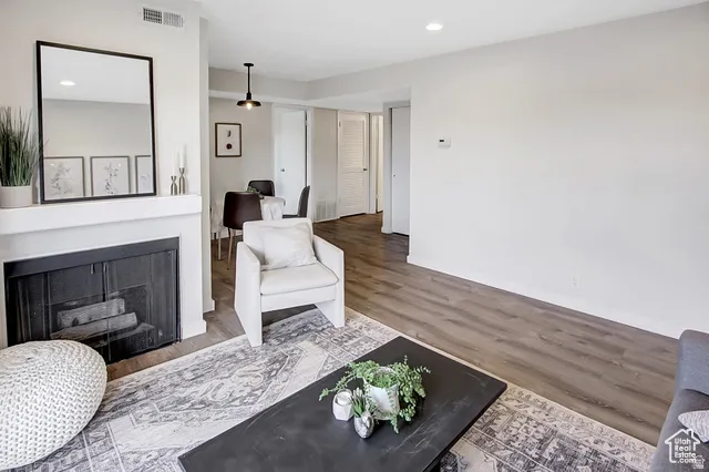 Wood-finish flooring throughout, featuring a white painted fireplace with a mantel, recessed lighting, and a modern ceiling fixture in the dining area