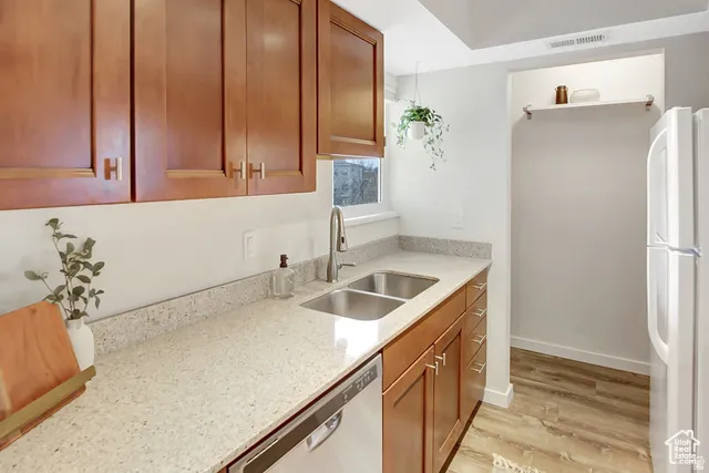 Wood-finish cabinetry, light-toned countertops, double basin sink with a high-arc faucet, integrated dishwasher, and wood-finish flooring