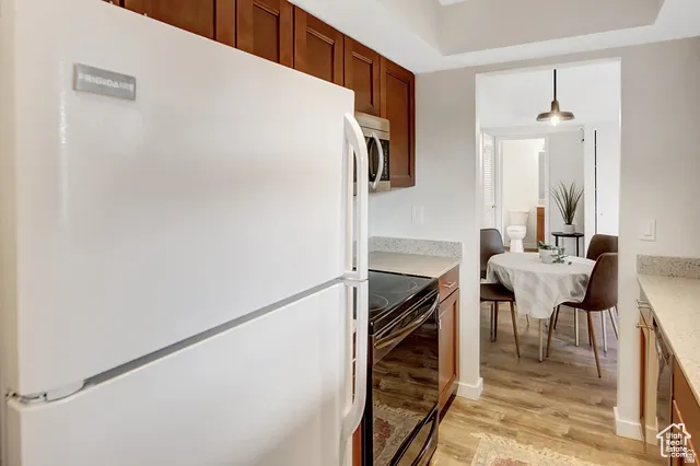 White refrigerator and built-in microwave, wood-finish cabinetry, speckled countertops, and wood-look flooring