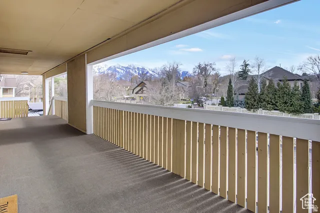 Expansive covered balcony featuring a light wood railing and a durable carpeted surface