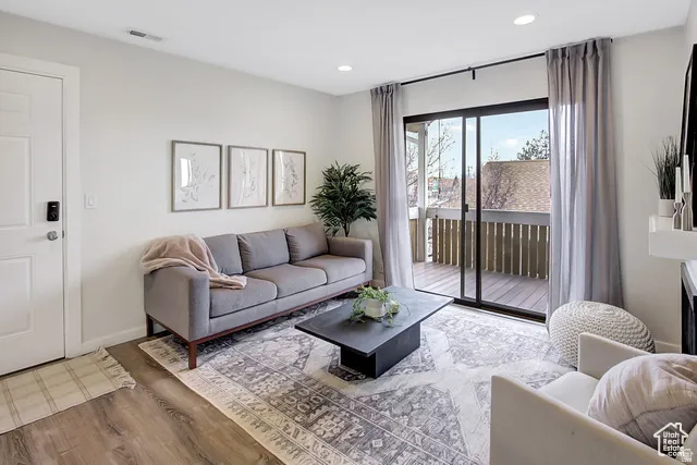 Wood-finish flooring, recessed lighting, white interior door, dark-framed sliding glass door, and an exterior wood deck