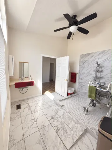 Vaulted ceiling with a ceiling fan, tiled flooring, a walk-in shower with tiled walls, and a wall-mounted vanity