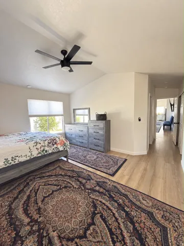 Vaulted ceiling with a modern ceiling fan, wood-finish flooring, and natural light from a large window