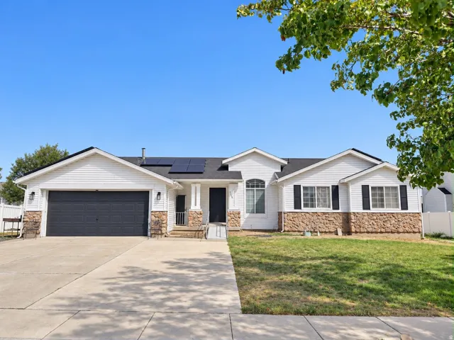 White siding exterior with stone accents, dark shingles, an attached two-car garage, and solar panels