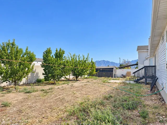 Expansive backyard featuring mature trees, a concrete patio, a wooden deck with dark railing, a shed, and mountain scenery