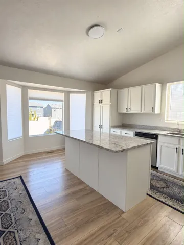 Kitchen featuring a center island with a light-toned countertop, wood-finish flooring, white cabinetry, and a bay window