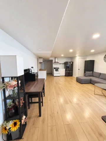 Recessed lighting, wood-finish flooring, white walls, and a visible kitchen area with stainless steel appliances