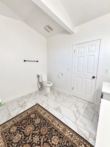 White tile flooring with subtle veining, ceiling beam, and a white paneled door with a black doorknob