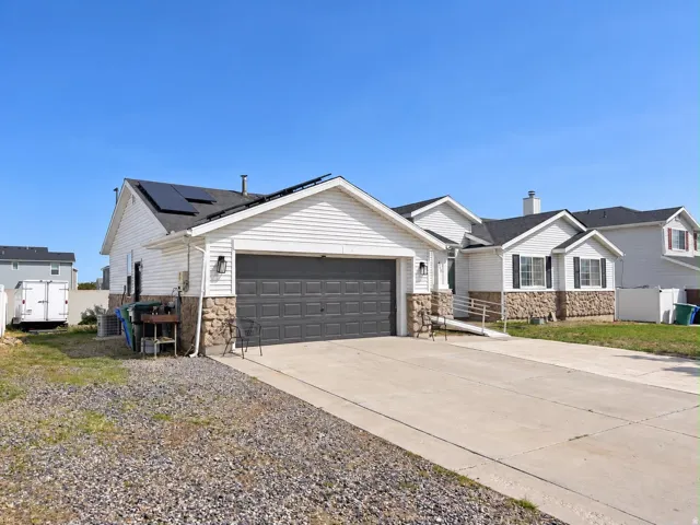 Exterior featuring white siding, stone veneer accents, a dark gray garage door, solar panels, and a concrete driveway