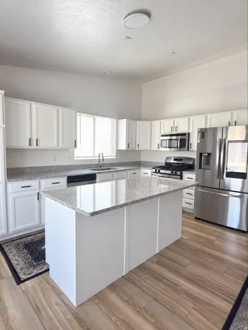 White cabinetry with black hardware, stone countertops, stainless steel appliances, wood-finish flooring, and a central island