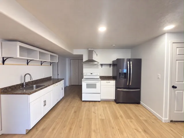 Kitchen featuring wood-finish flooring, white cabinetry, integrated stainless steel sink, a stainless steel range hood, and recessed lighting
