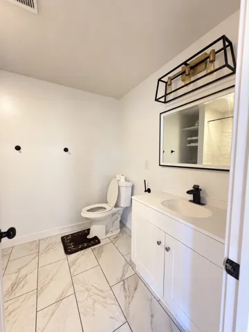 White vanity with integrated sink, black faucet, and framed mirror with integrated lighting
