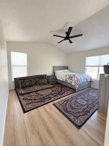 Vaulted ceiling, wood-finish flooring, dual windows, ceiling fan, and neutral wall tones