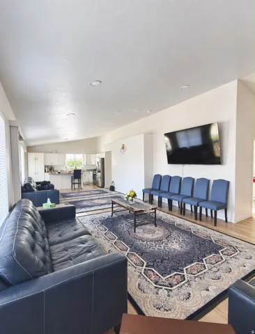Open-concept living area featuring light wood-finish flooring, recessed lighting, and a white kitchen with stainless steel appliances