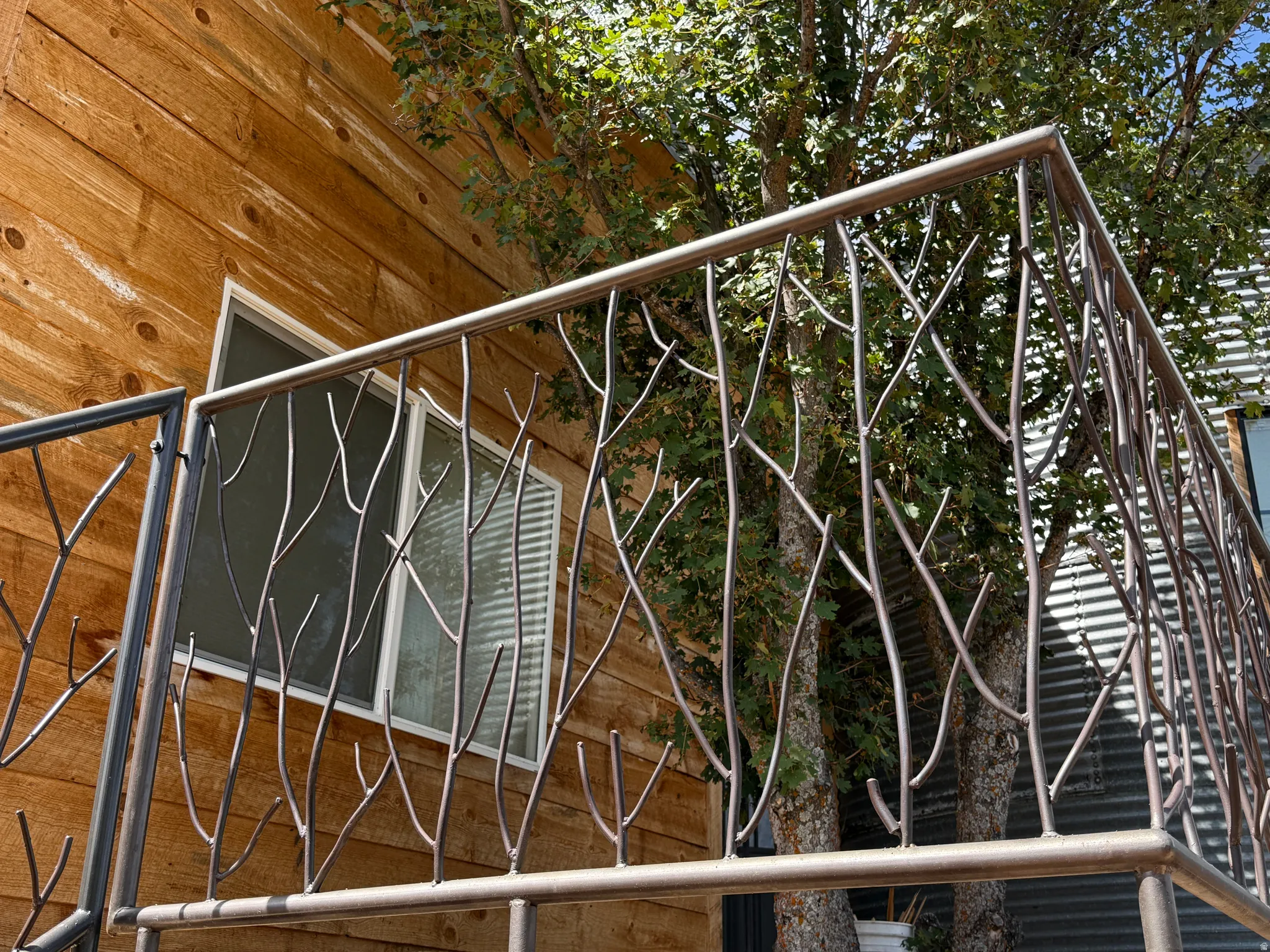 Custom metalwork railing with a branch motif, light-toned wood siding, and a white-framed window