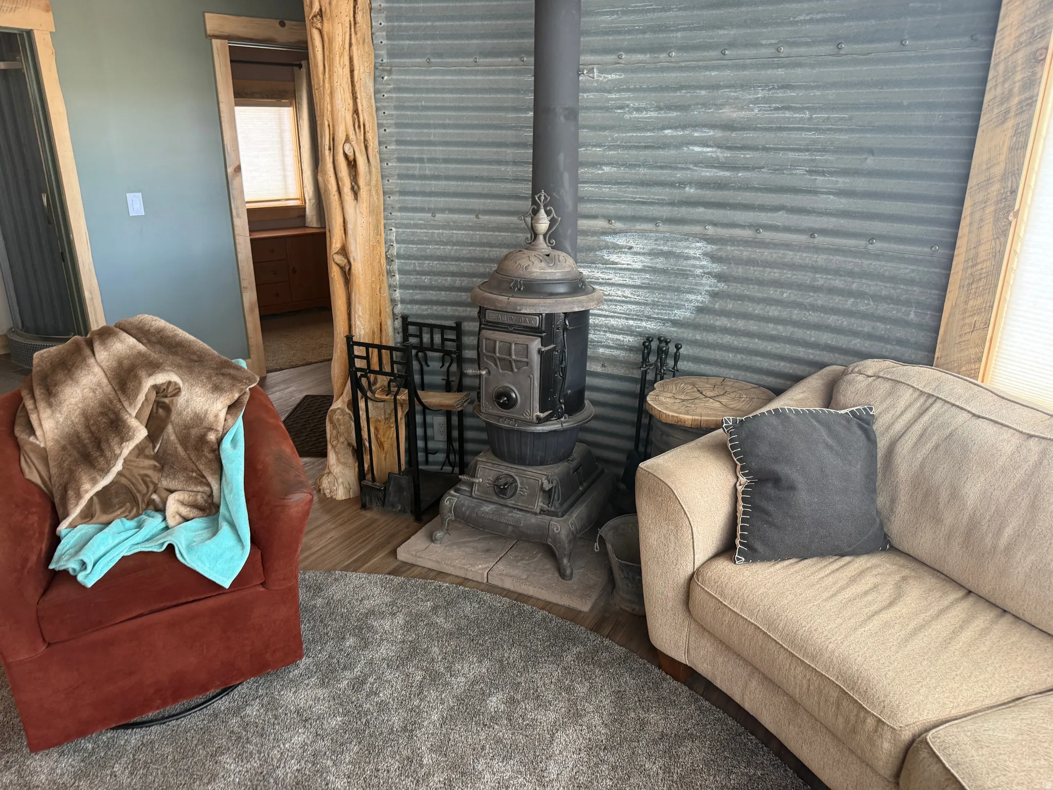 Cast iron wood-burning stove with a metal flue, corrugated metal accent wall, and wood-finish flooring