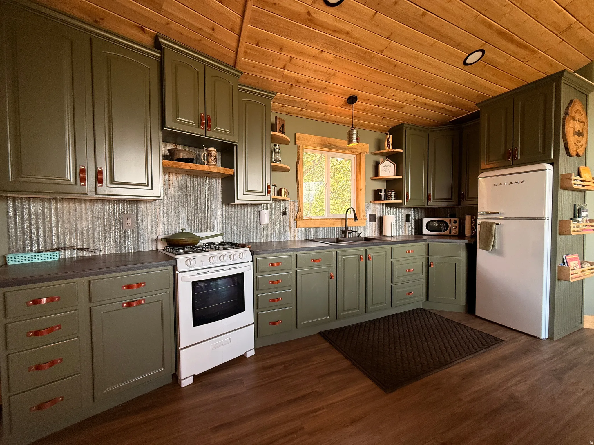 Wood-finish flooring, wood-paneled ceiling, integrated wall cabinetry with drawer pulls, textured metal backsplash, and a window with trim