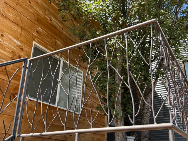 Custom metalwork railing with a branch motif, light-toned wood siding, and a white-framed window