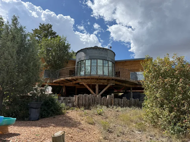 Wood-sided exterior featuring an elevated circular balcony, full-height windows, and a metal-clad architectural element