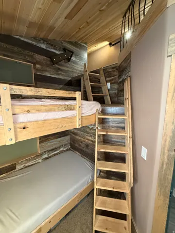 Wood-clad ceiling, bunk beds with wood frames, wood-finish wall paneling, and a wood ladder providing access to a loft space