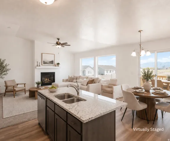 Open-concept living space featuring wood-finish flooring, a kitchen island with stone-finish countertop, a built-in fireplace, and large windows