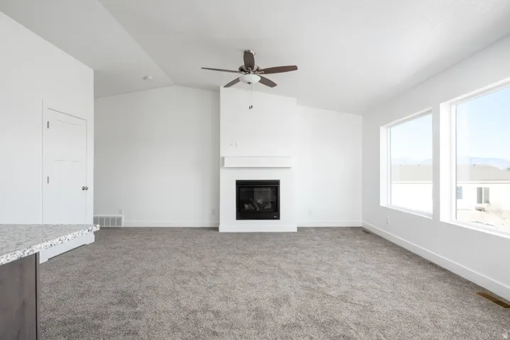 Vaulted ceiling, white walls, integrated fireplace, ceiling fan, and large windows
