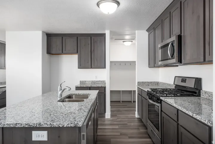 Kitchen featuring granite countertops, dark wood-finish cabinetry, stainless steel appliances, and a double basin sink