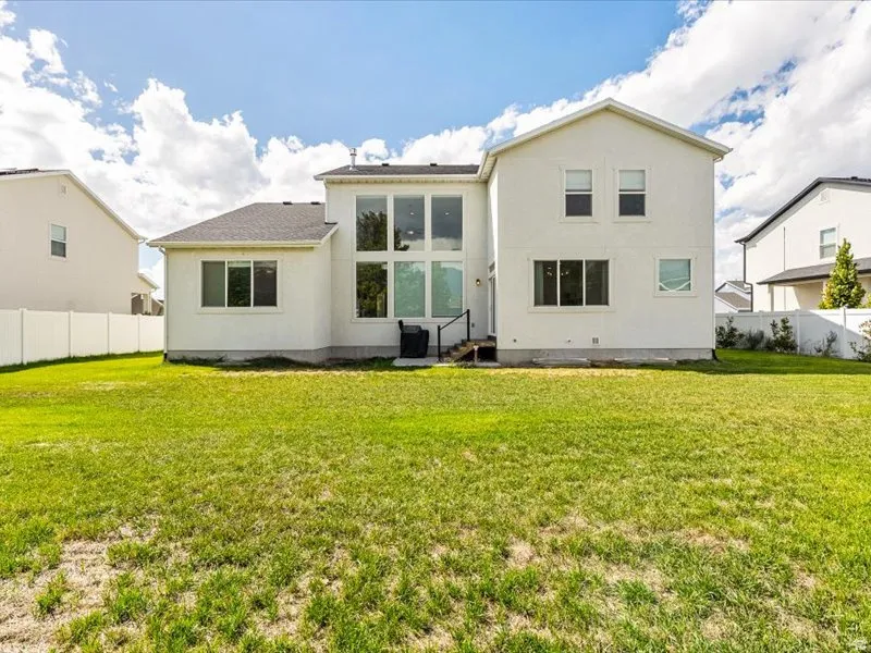 Expansive backyard featuring a lush lawn, white privacy fencing, and a contemporary white stucco exterior