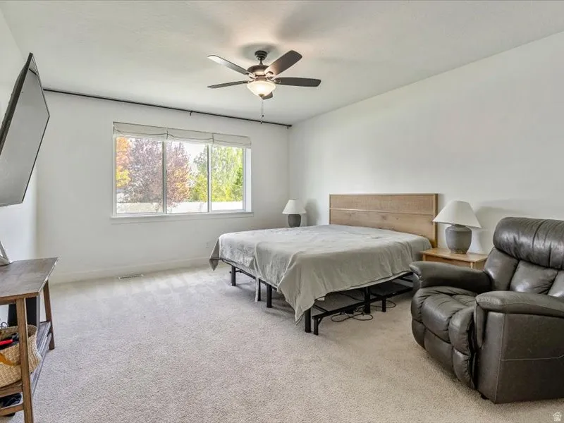 Spacious room with plush carpeting, a large window, and ceiling fan with integrated lighting