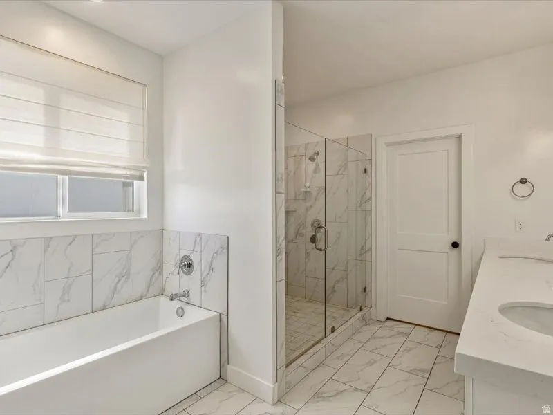 Bathtub with marble-patterned tile surround, glass-enclosed shower, and a vanity with an integrated sink