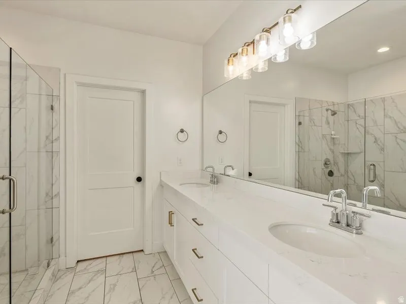 Double vanity with undermount sinks, stone countertops, a large mirror, a multi-bulb vanity light fixture, and tile flooring