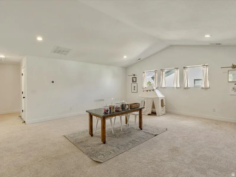 Vaulted ceilings with recessed lighting, three windows providing natural light, wall-to-wall carpeting, and a neutral color palette