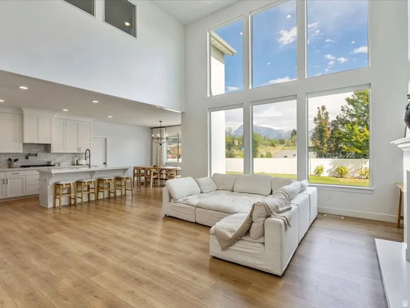 Two-story ceilings, expansive window wall, wood-finish flooring, island kitchen with white cabinetry, and a formal dining area
