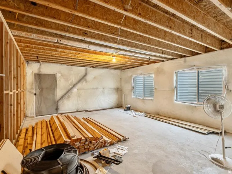 Unfinished space featuring exposed ceiling joists, concrete flooring, framed wall sections, and two window openings