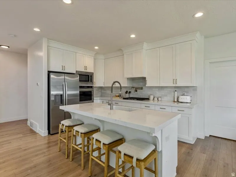 Kitchen featuring white shaker cabinetry, stainless steel appliances, a center island with countertop seating, and wood-finish flooring