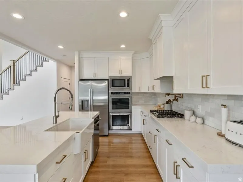 White shaker cabinetry with gold-tone hardware, stainless steel appliances, wood-finish flooring, and subway tile backsplash