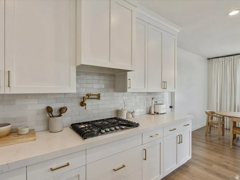 White shaker cabinetry with brass hardware, light-toned countertops, subway tile backsplash, and wood-finish flooring