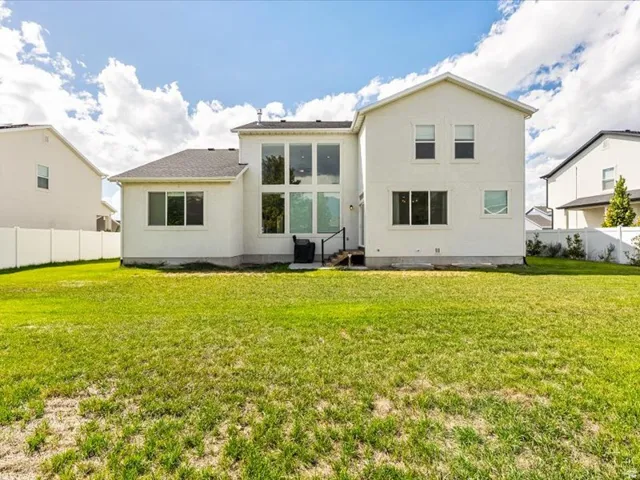 Expansive backyard featuring a lush lawn, white privacy fencing, and a contemporary white stucco exterior