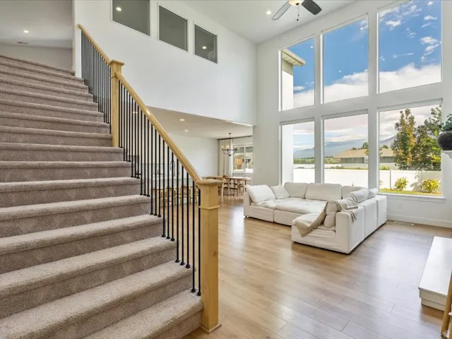 Two-story living area with expansive floor-to-ceiling windows, wood-finish flooring, and a contemporary staircase featuring a wood handrail and black metal balusters