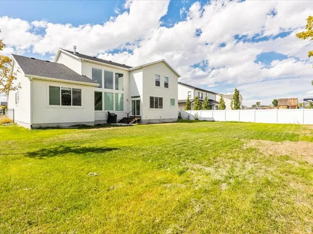 Expansive backyard with a manicured lawn, white privacy fencing, and a contemporary exterior featuring multiple large windows