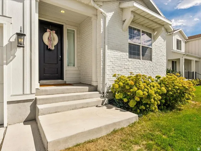 White brick exterior with board and batten accents, a black paneled entry door, and concrete steps