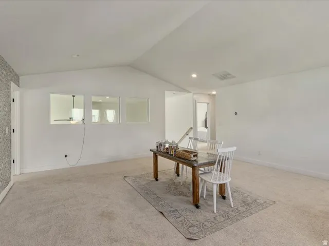 Vaulted ceiling, carpeted flooring, wall-mounted light fixtures, interior window openings, and a solid core door