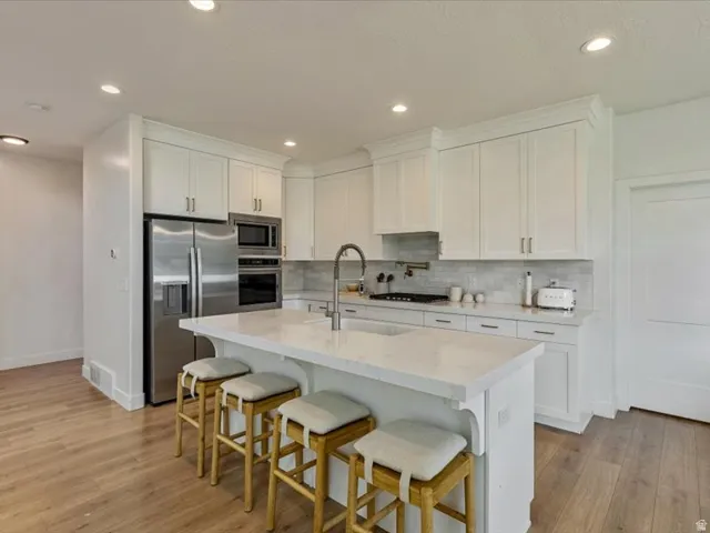 Kitchen featuring white shaker cabinetry, stainless steel appliances, a center island with countertop seating, and wood-finish flooring